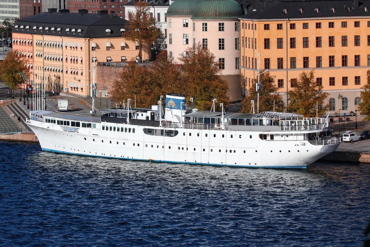 White floating hotel ship moored along a riverbank in autumn