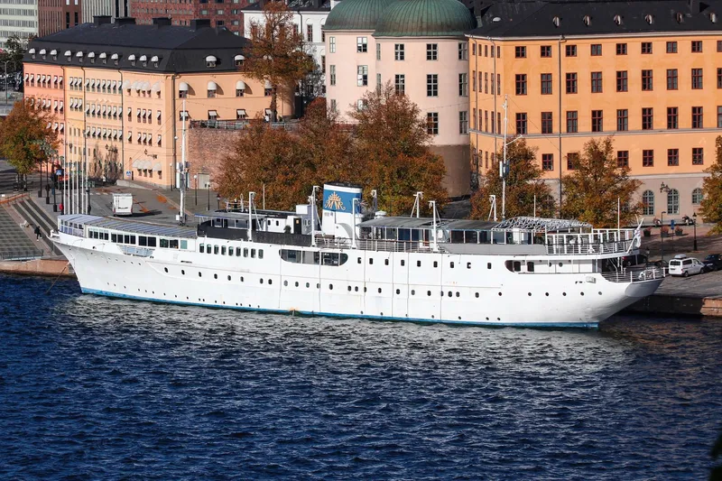 White floating hotel ship moored along a riverbank in autumn