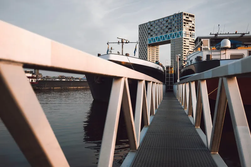 A floating botel moored along an urban river embankment with a pedestrian gangway