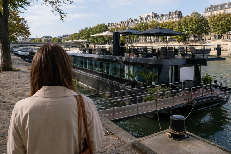 A converted barge hotel moored along an urban river embankment in Paris