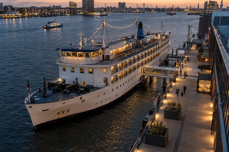 A moored hotel ship docked along a European urban waterfront at dusk