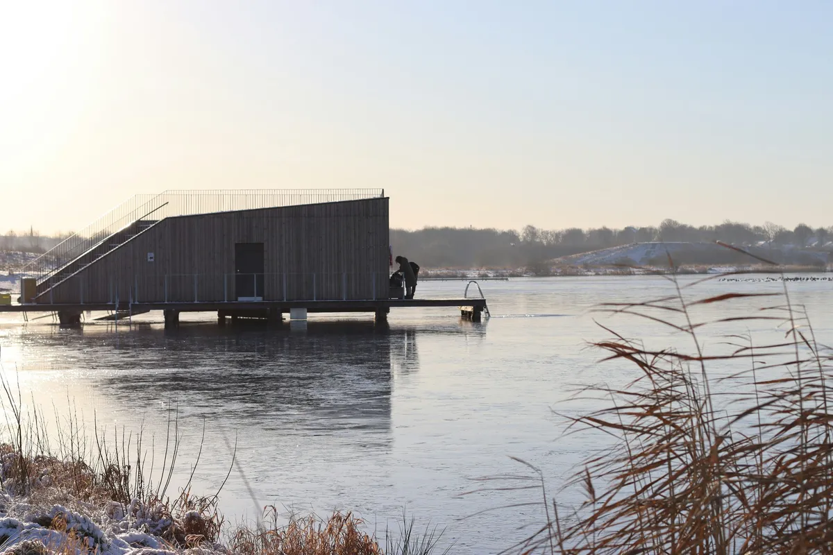 Wooden floating sauna with a cold plunge ladder on a frozen Nordic lake